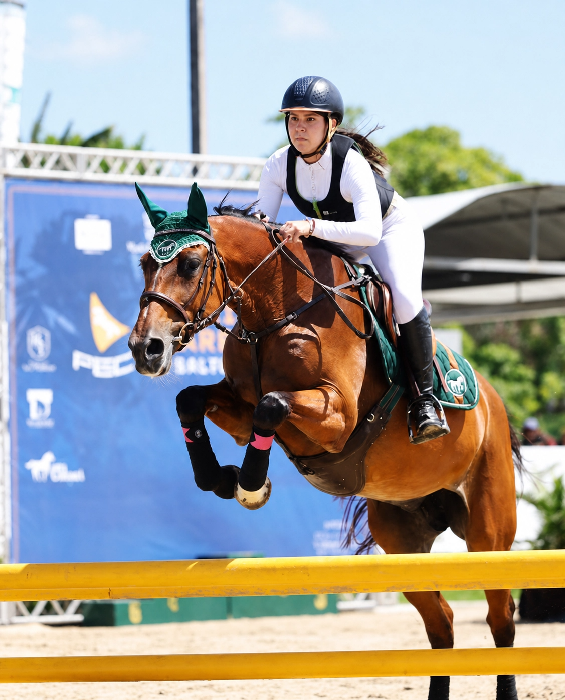 Amazona saltando obstáculo amarelo em competição de hipismo