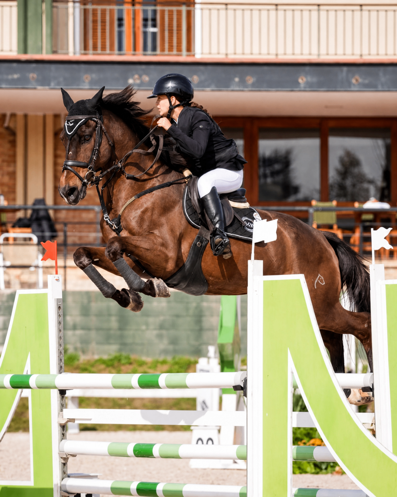 Cavaleira saltando obstáculo verde e branco em pista